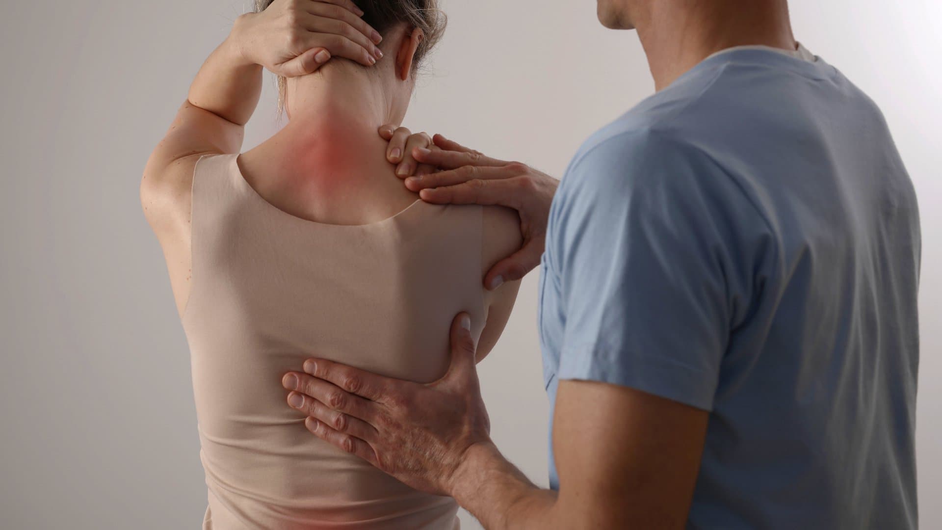 A practitioner's hands on a patient's shoulder blade and neck.