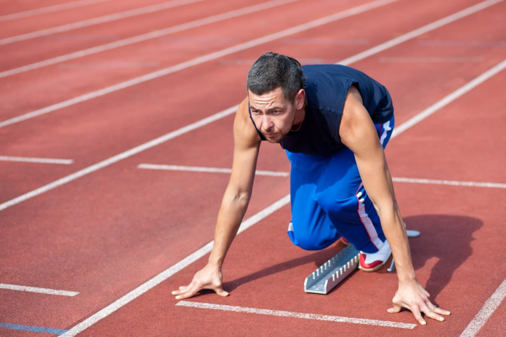 A man crouched at the start line of a running track.